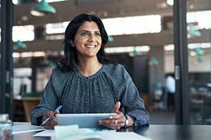 A quality professional excited about step 3 An executive smiling at their desk, holding a tablet